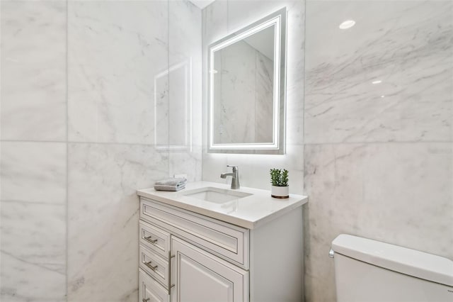 bathroom with vanity, toilet, and tile walls