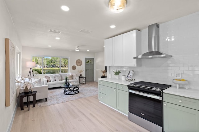 1443 Paloma Ln, Dunedin, FL 34698 - kitchen featuring stainless steel gas range oven, wall chimney range hood, light wood-type flooring, tasteful backsplash, and light countertops