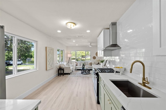 1443 Paloma Ln, Dunedin, FL 34698 - kitchen with wall chimney exhaust hood, stainless steel range with gas stovetop, a sink, backsplash, and light stone counters