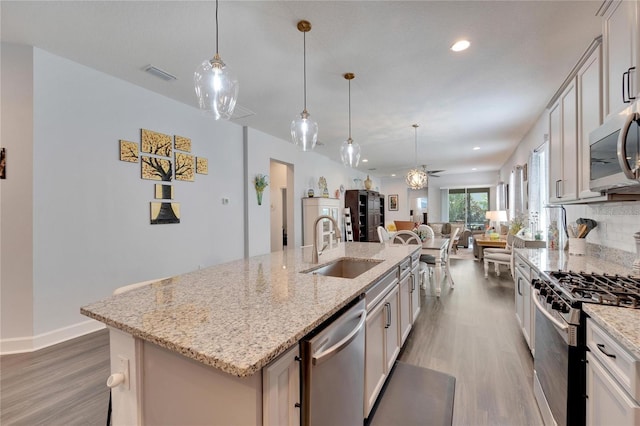 kitchen with a sink, stainless steel appliances, open floor plan, wood finished floors, and visible vents