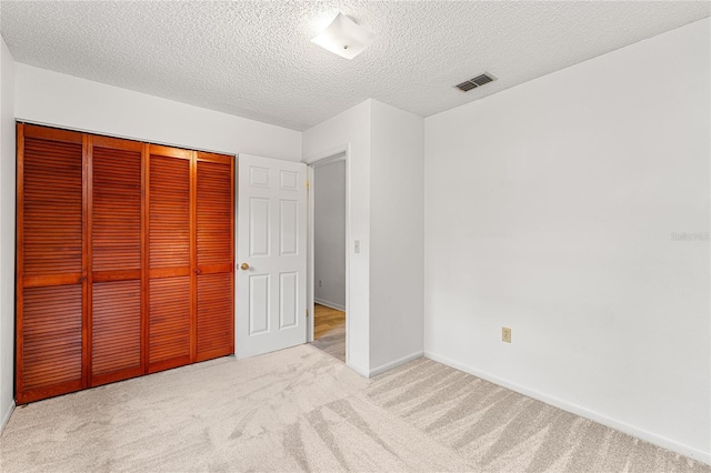 unfurnished bedroom featuring a textured ceiling, visible vents, carpet floors, baseboards, and a closet