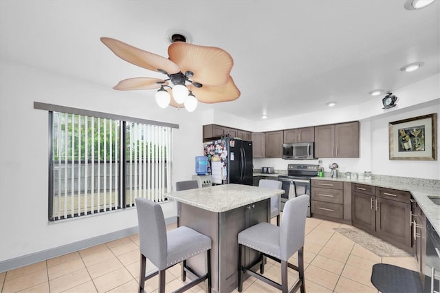 kitchen with dark brown cabinetry, appliances with stainless steel finishes, a kitchen breakfast bar, and light tile patterned floors