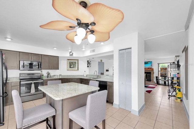 kitchen with a breakfast bar area, light tile patterned floors, a sink, a brick fireplace, and appliances with stainless steel finishes