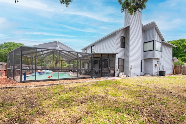 back of house with a chimney, fence, a lawn, a fenced in pool, and glass enclosure