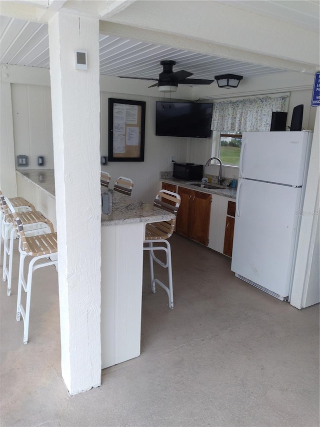 kitchen featuring a kitchen breakfast bar, a ceiling fan, light colored carpet, a sink, and freestanding refrigerator