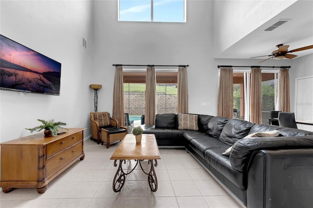 living area with light tile patterned flooring, ceiling fan, visible vents, and a towering ceiling