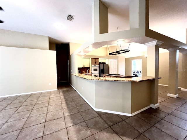 kitchen featuring visible vents, freestanding refrigerator, tile patterned flooring, a peninsula, and light stone countertops