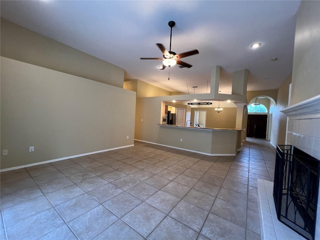 unfurnished living room with light tile patterned flooring, ceiling fan, a fireplace, arched walkways, and vaulted ceiling
