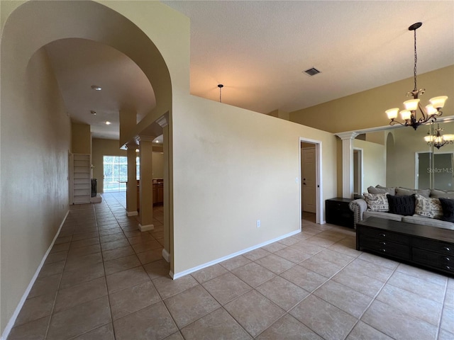interior space featuring arched walkways, baseboards, decorative columns, and light tile patterned floors