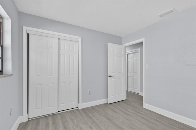 unfurnished bedroom with baseboards, light wood-type flooring, visible vents, and a closet