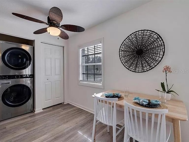 laundry area with laundry area, a ceiling fan, baseboards, wood finished floors, and stacked washer and clothes dryer