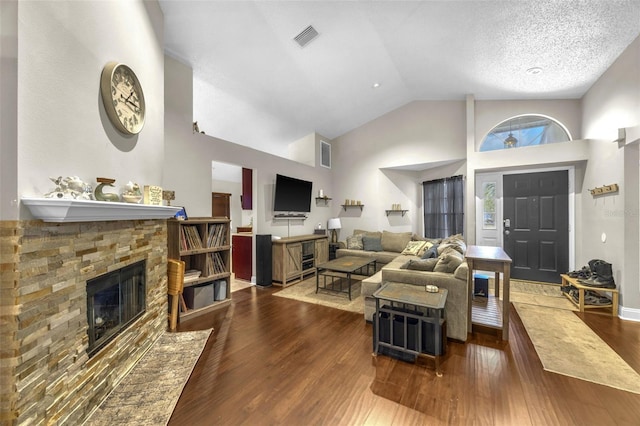 living room with high vaulted ceiling, wood finished floors, a stone fireplace, and visible vents