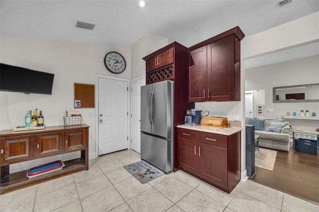 kitchen featuring visible vents, light countertops, light tile patterned floors, freestanding refrigerator, and reddish brown cabinets