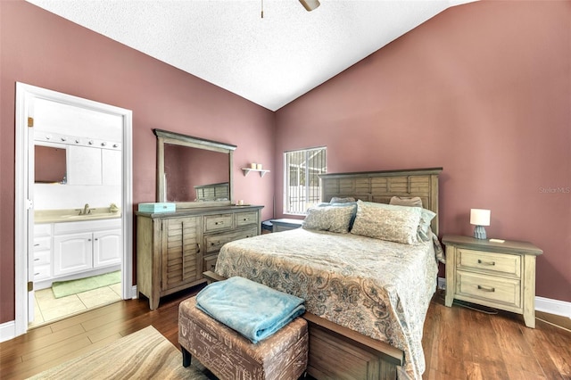 bedroom featuring wood finished floors, baseboards, a textured ceiling, connected bathroom, and vaulted ceiling