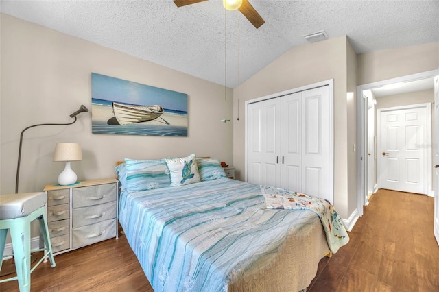 bedroom with a textured ceiling, wood finished floors, vaulted ceiling, visible vents, and a closet