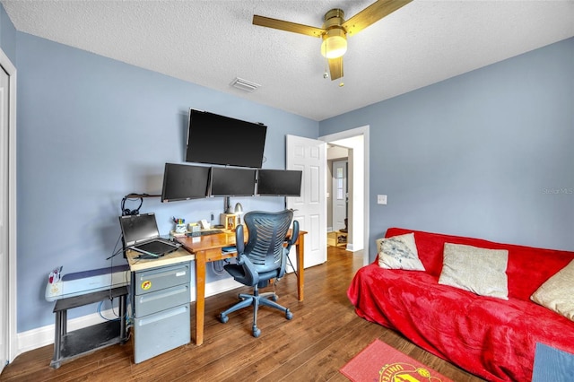 office featuring visible vents, wood finished floors, baseboards, ceiling fan, and a textured ceiling