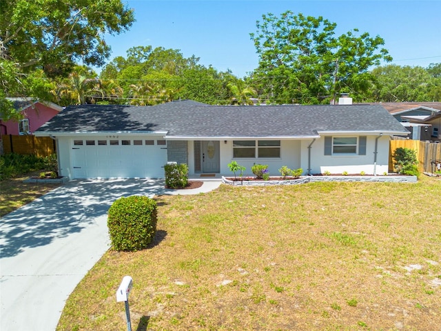 ranch-style house with a front yard, fence, concrete driveway, an attached garage, and a shingled roof