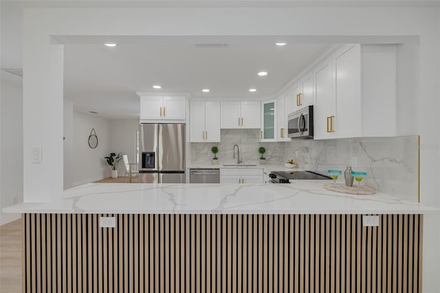 kitchen with a peninsula, light stone countertops, a sink, backsplash, and stainless steel appliances