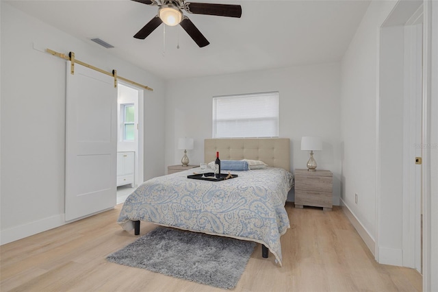 bedroom featuring baseboards, visible vents, a barn door, and light wood-type flooring