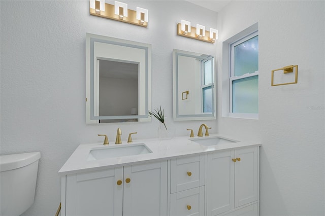 bathroom featuring double vanity, toilet, and a sink