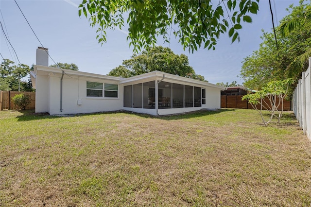 rear view of house with a lawn, a fenced backyard, a chimney, and a sunroom