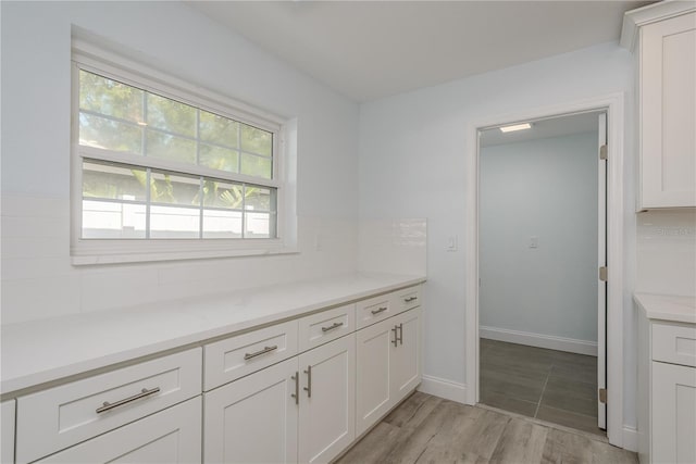1152 Jackmar Rd, Dunedin, FL 34698 - kitchen featuring white cabinets, light countertops, light wood finished floors, backsplash, and baseboards