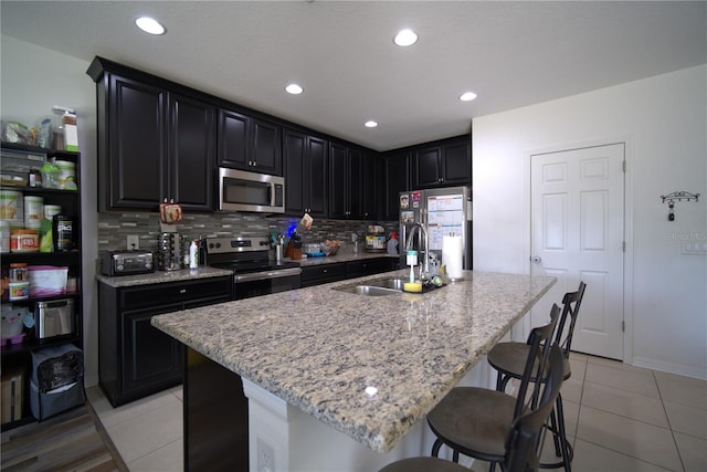 kitchen featuring appliances with stainless steel finishes, a sink, dark cabinetry, a kitchen breakfast bar, and light tile patterned floors