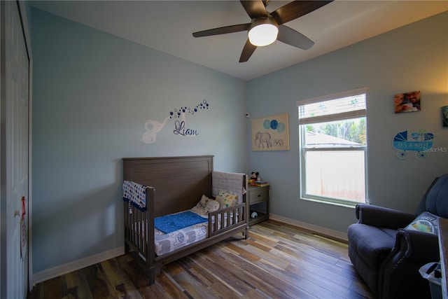 bedroom with baseboards, a ceiling fan, a crib, and wood finished floors