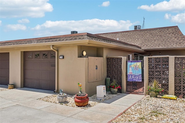 exterior space with a gate, a garage, stucco siding, a shingled roof, and driveway