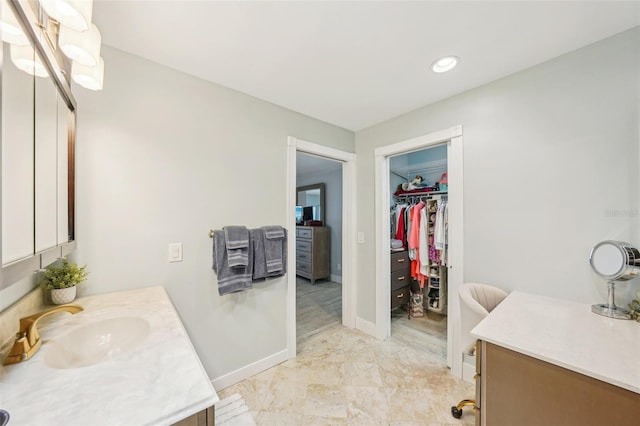 bathroom featuring baseboards, vanity, recessed lighting, and a walk in closet