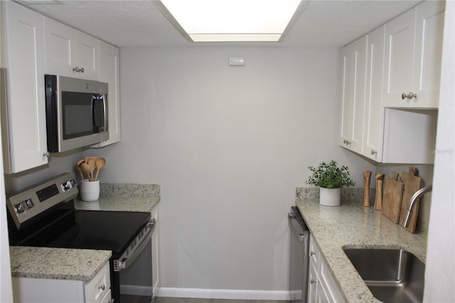 kitchen featuring a sink, appliances with stainless steel finishes, white cabinets, and light stone countertops