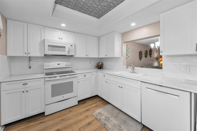 kitchen with white appliances, a sink, a tray ceiling, recessed lighting, and light wood-style flooring