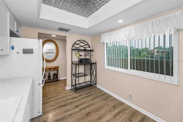 hall with a raised ceiling, wood finished floors, baseboards, recessed lighting, and a sink
