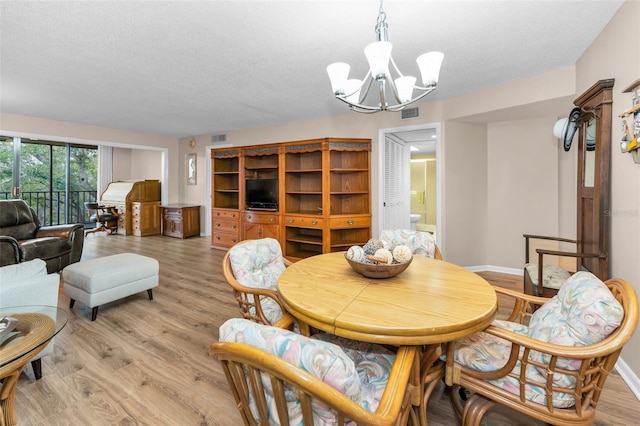 dining room featuring a chandelier, light wood-style flooring, a textured ceiling, and baseboards