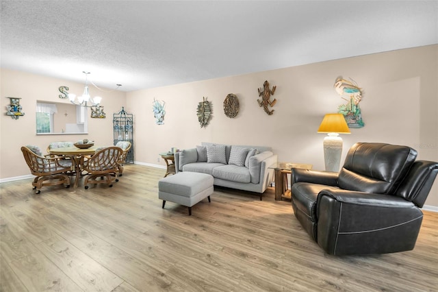 living area with light wood-type flooring, a chandelier, baseboards, and a textured ceiling