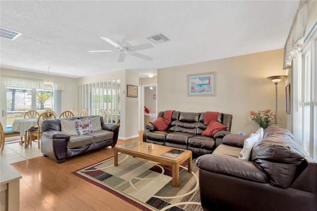 living room featuring a ceiling fan, a textured ceiling, visible vents, and light wood-style floors