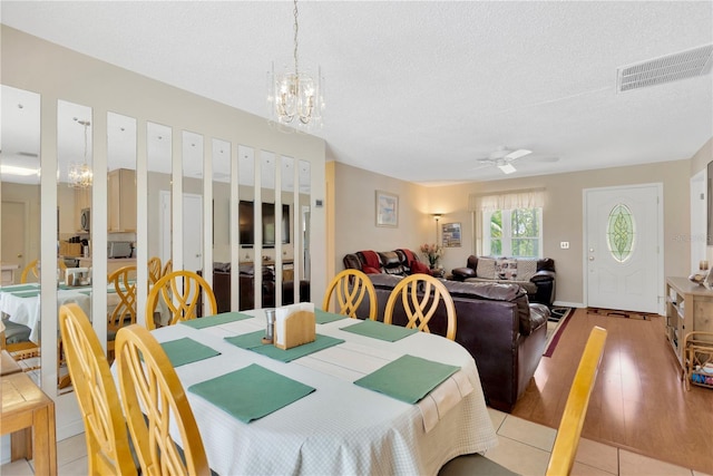 dining area featuring visible vents, a textured ceiling, ceiling fan with notable chandelier, and light tile patterned floors