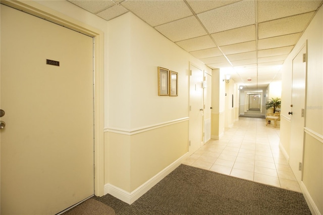 corridor with light colored carpet, baseboards, light tile patterned floors, and a drop ceiling