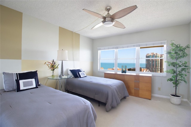 bedroom with baseboards, a ceiling fan, a textured ceiling, and light colored carpet