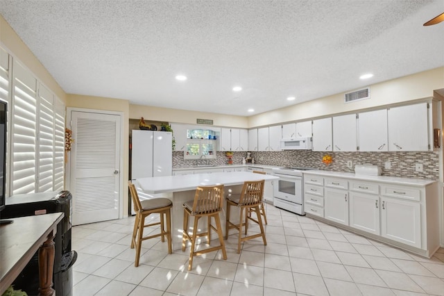 kitchen with decorative backsplash, visible vents, a sink, light countertops, and white appliances