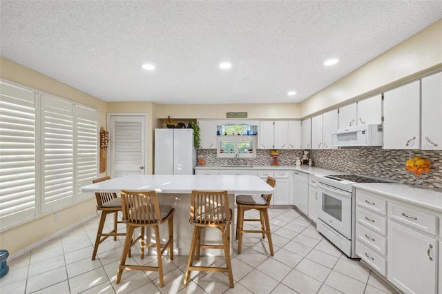 kitchen with backsplash, a kitchen bar, a sink, light tile patterned floors, and white appliances