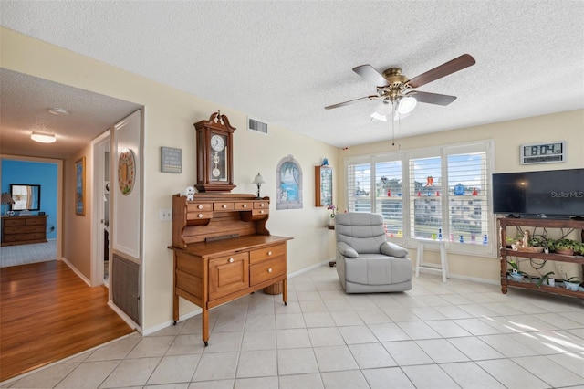 living area featuring a textured ceiling, a ceiling fan, baseboards, light tile patterned floors, and visible vents