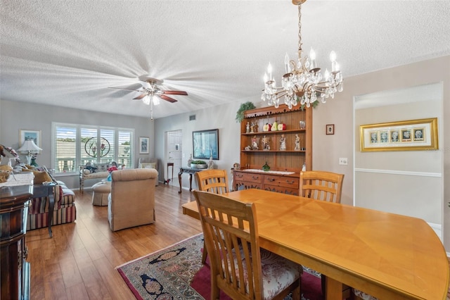 dining area with light wood-style floors, ceiling fan with notable chandelier, a textured ceiling, and visible vents