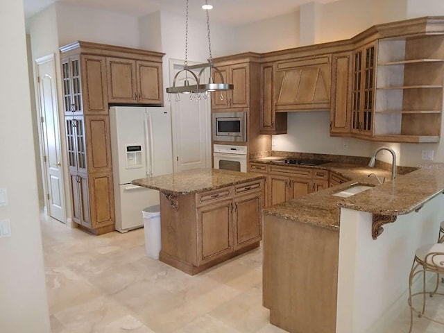 kitchen with stone counters, a sink, brown cabinetry, a kitchen breakfast bar, and white appliances