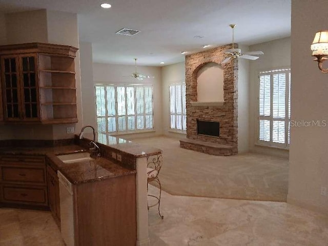 kitchen with a sink, open floor plan, a stone fireplace, ceiling fan, and light colored carpet