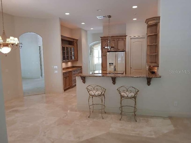 kitchen featuring a breakfast bar, open shelves, an inviting chandelier, arched walkways, and fridge with ice dispenser