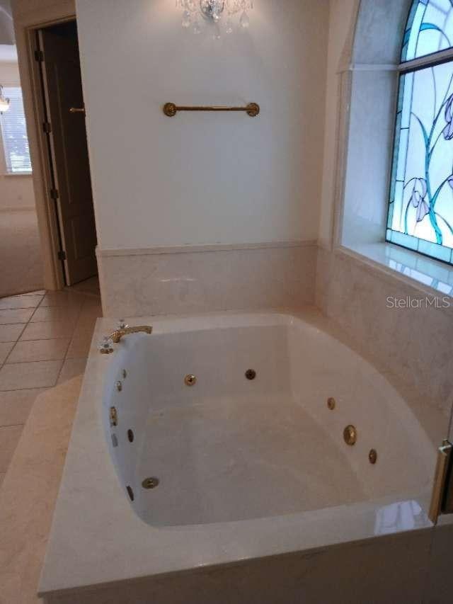 full bath featuring a notable chandelier, tile patterned flooring, and a whirlpool tub