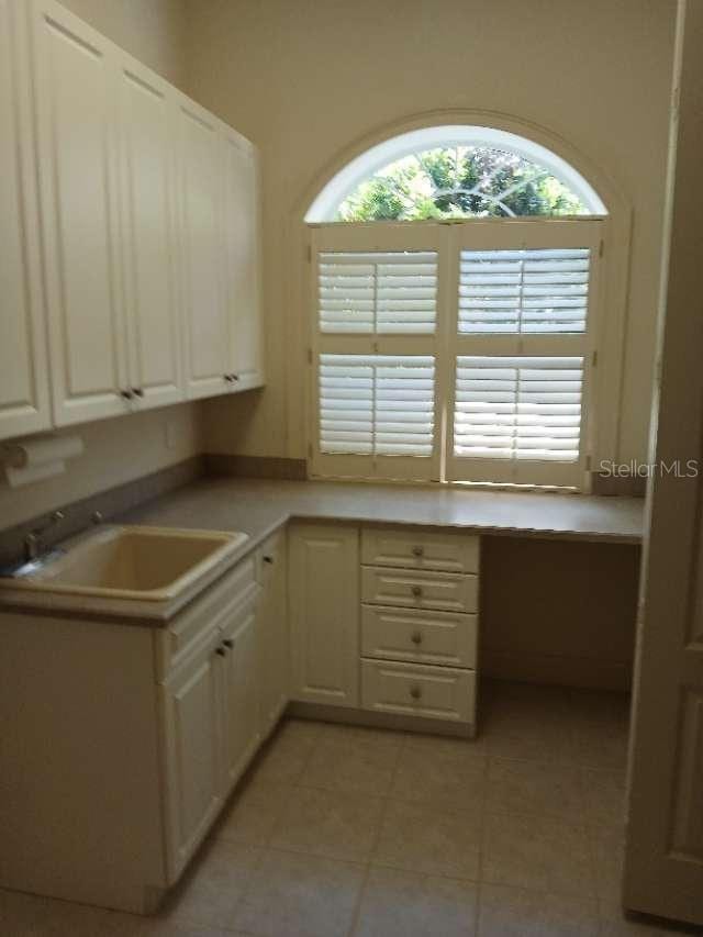 kitchen with light tile patterned flooring, built in study area, a sink, white cabinetry, and light countertops