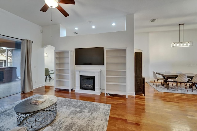 16516 Bridgewalk Dr, Lithia, FL 33547 - living room with wood finished floors, a ceiling fan, visible vents, arched walkways, and a glass covered fireplace