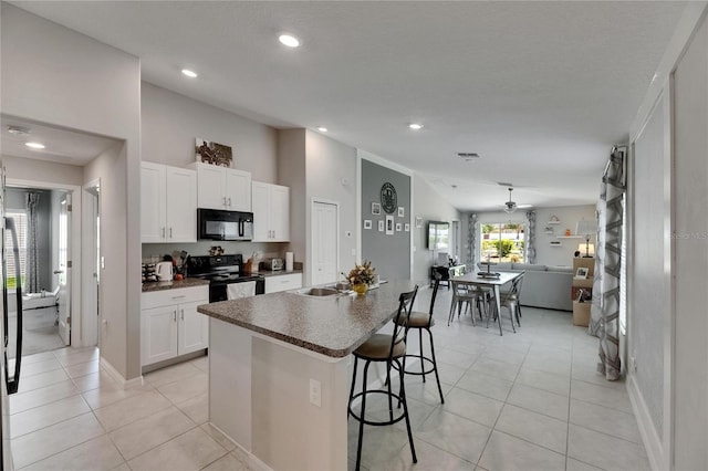 11707 Sunburst Marble Rd, Riverview, FL 33579 - kitchen with black appliances, open floor plan, dark countertops, a breakfast bar area, and white cabinetry